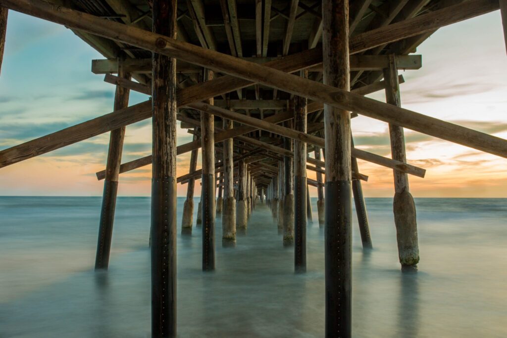 Photo of wooden pier stretching out into calm water towards the horizon, supported by large beams rising vertically and diagonally.